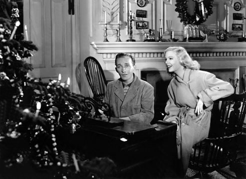 Bing Crosby and Marjorie Reynolds sing by a fire-lit piano in <em>White Christmas<em>